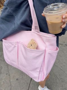 a person holding a pink bag with a teddy bear in the pocket and a drink