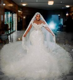 a woman in a white wedding gown and veil with feathers on the skirt is walking through a hall