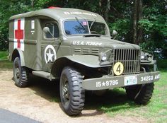 an army truck is parked on the side of the road in front of some trees