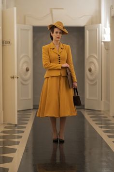 a woman in a yellow dress and hat is walking down the hall with her purse