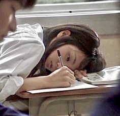 a woman sitting at a desk writing on a piece of paper with a pen in her hand