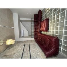 an empty room with red leather couches and white tiles on the walls, in front of a staircase