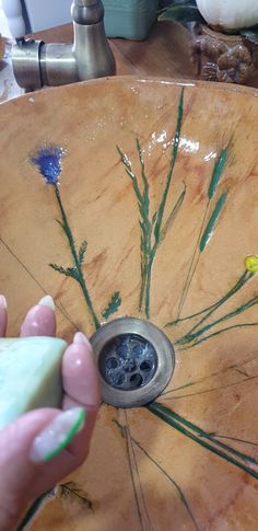 a person is holding an object in their hand near a sink with flowers on it