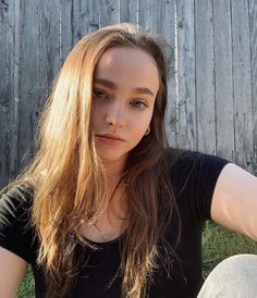 a woman sitting in the grass with her hand on her hip and looking at the camera