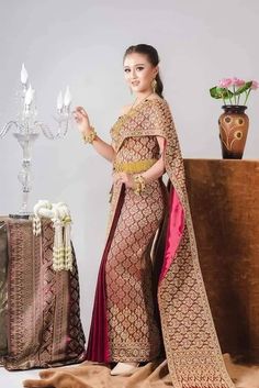 a woman standing next to a table with a vase on it and wearing a red and gold sari