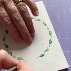 someone is doing something with their hand on top of a piece of paper that has holly leaves drawn on it