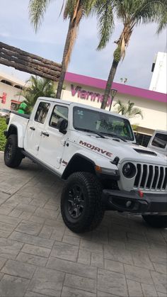 a white jeep is parked in front of a building with palm trees and a pink sign