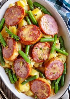 a white bowl filled with green beans, potatoes and kielbasa on top of a wooden table