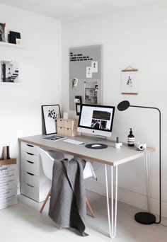 a desk with a computer, lamp and other items on top of it in a white room