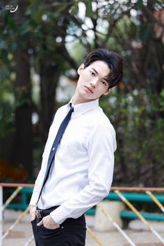 a young man wearing a white shirt and black tie standing in front of some trees