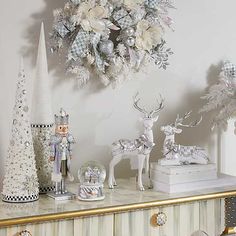 christmas decorations and ornaments on a dresser in front of a wall with a wreath hanging above it