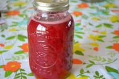 a jar filled with red liquid sitting on top of a flowery tablecloth covered table