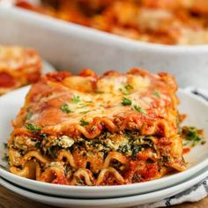 a white plate topped with lasagna covered in cheese and sauce next to a casserole dish