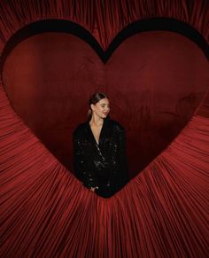 a woman standing in front of a heart shaped red curtain with her hands on her hips