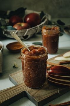 a jar filled with food sitting on top of a wooden cutting board next to apples