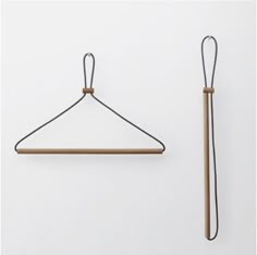 a pair of clothes hangers on a white wall next to a black string and wooden stick