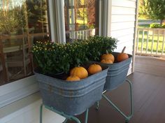 two metal planters filled with pumpkins on a porch