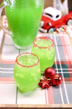 two glasses filled with green liquid sitting on top of a table next to a christmas ornament