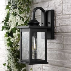 a black outdoor wall light next to a white brick wall with ivy growing on it