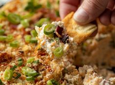 a person is dipping some food into a casserole with cheese and green onions