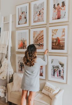 a woman standing in front of a wall with pictures on it and holding her hand up