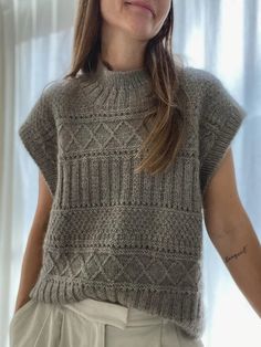 a woman standing in front of a window wearing a sweater