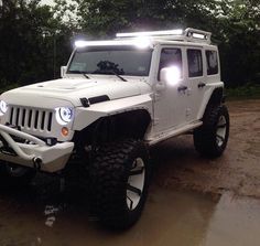 a white jeep is parked in the mud with its lights on and headlamps on