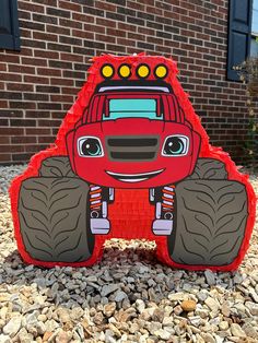 a large red monster truck sitting on top of a pile of rocks next to a brick building