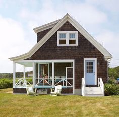 a small house with a porch and white railings on the front lawn, next to a grassy yard