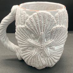 a white ceramic mug with an intricate design on the outside and inside, sitting on a gray surface