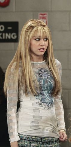 a woman with long blonde hair standing in front of a brick wall