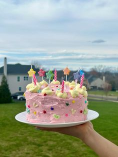 a hand holding a cake with pink frosting and candles