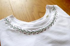 a white t - shirt with red and green thread on the collar is sitting on a wooden floor