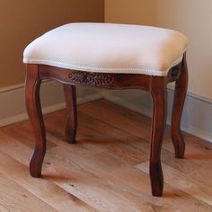 a wooden bench with a white cushion on it's seat in front of a wall