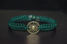 a green beaded bracelet with a gold sun charm on it's end, sitting on a black surface