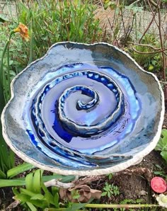 a blue and white bowl sitting in the middle of some grass with flowers around it