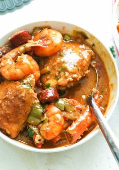 a bowl filled with shrimp and vegetables on top of a white tablecloth next to a spoon