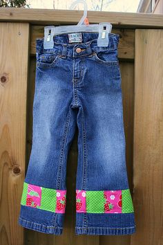 a pair of blue jeans hanging on a wooden fence with pink flowers and green polka dots