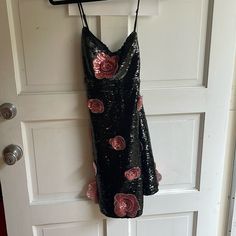 a black dress with pink flowers hanging on a door hanger in front of a white door