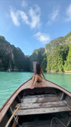 a woman is sitting in the bow of a boat looking out at the water and mountains