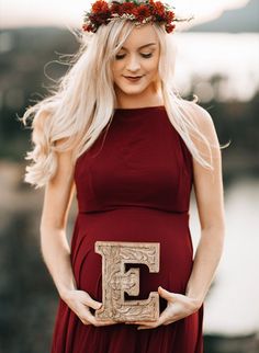 a pregnant woman in a red dress holding a wooden letter