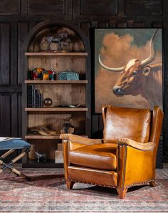 a living room with a cow painting on the wall next to a leather chair and ottoman