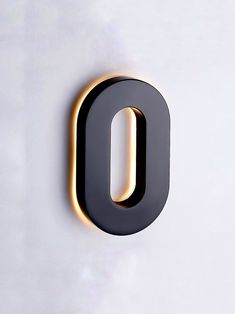 the letter o is lit up in black and gold on a white wall with a light at the end