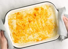 someone holding a casserole dish with cheese in it on a white counter top