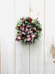 a christmas wreath hanging on the side of a white wooden wall with holly and red berries