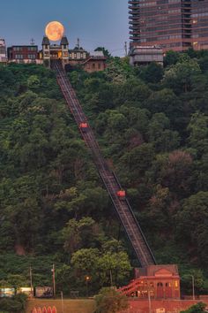 a train is going up the side of a hill with trees and buildings in the background