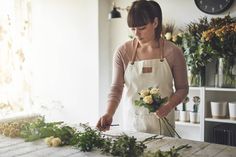 a woman in an apron arranging flowers on a table