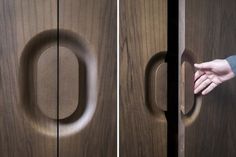 a person's hand opening a wooden door with an oval handle on the left and right side