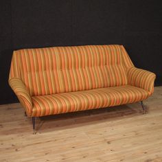 an orange and yellow striped couch sitting on top of a hard wood floor next to a black wall