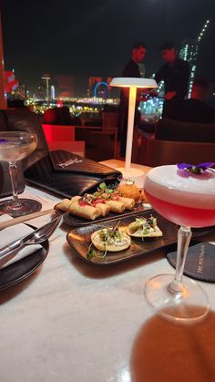 food and drinks on a table at a restaurant with a view of the city in the background